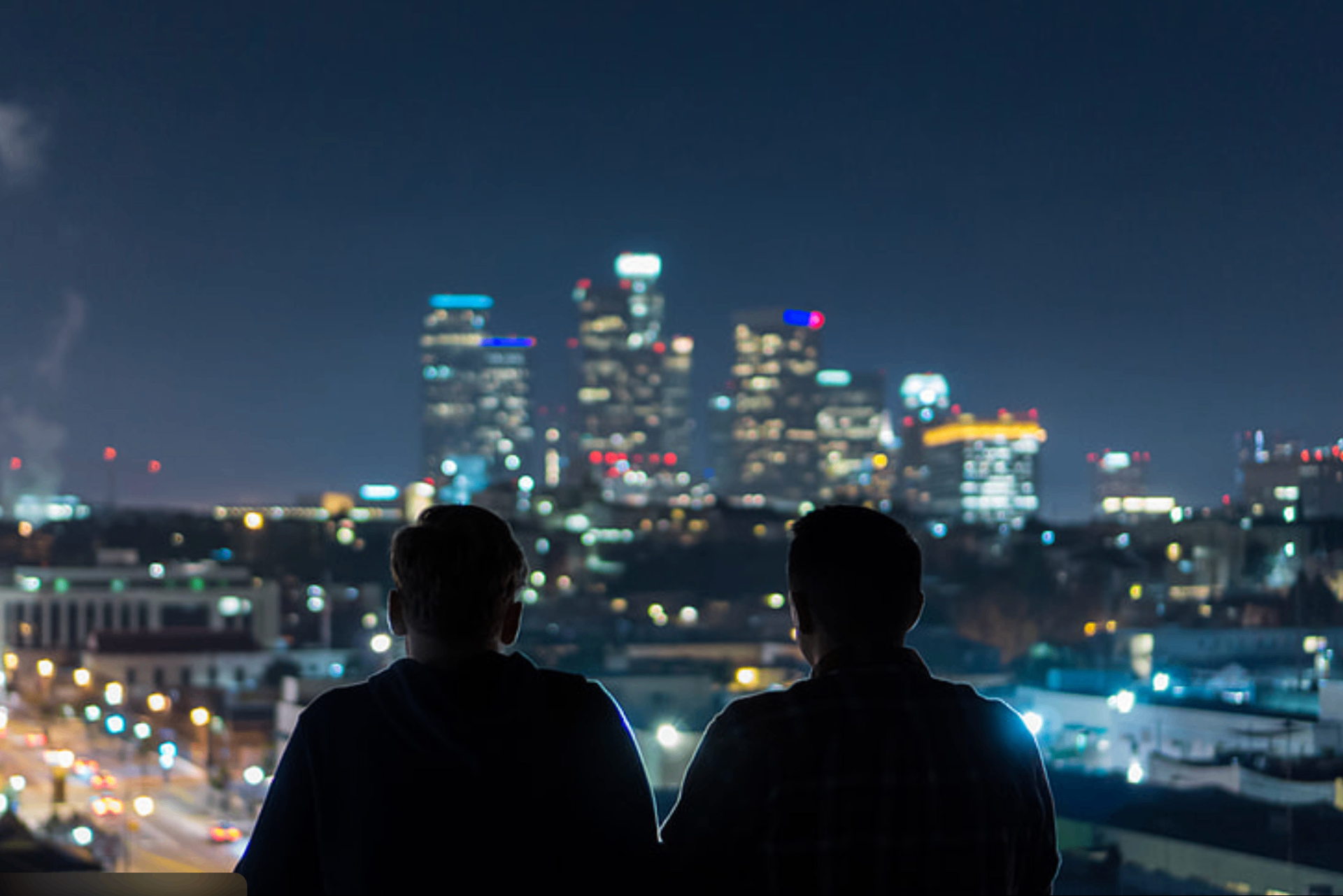 Two silhouettes overlooking a city skyline at night